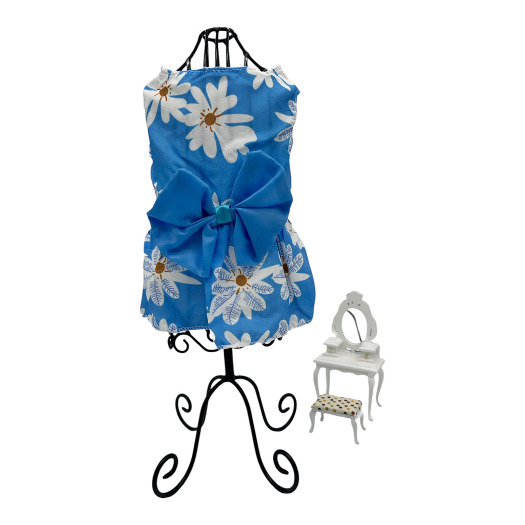 Blue cat dress with white floral patterns on a black stand, with a small white chair in the background.