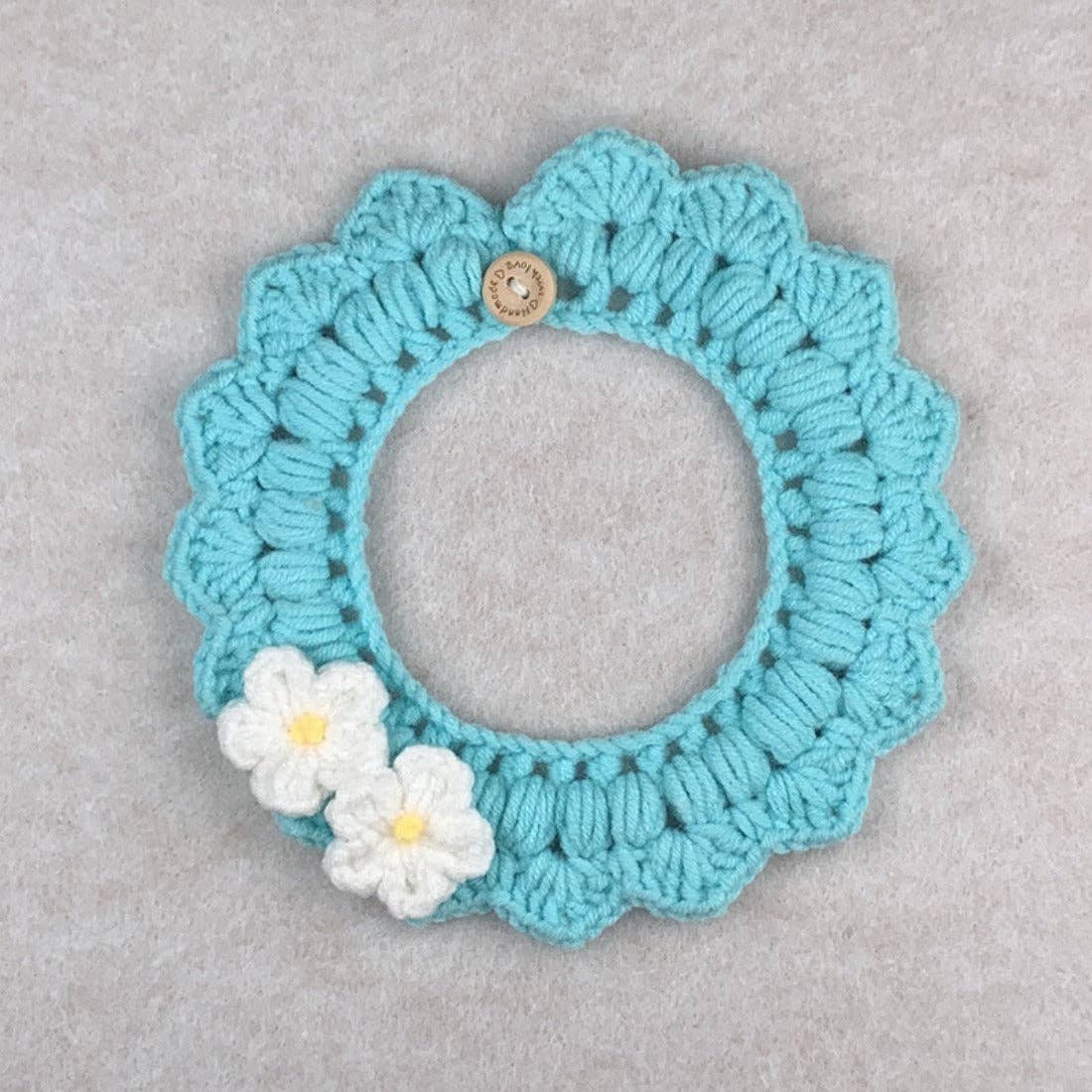 Crocheted teal circular cat collar with white flowers on a gray background