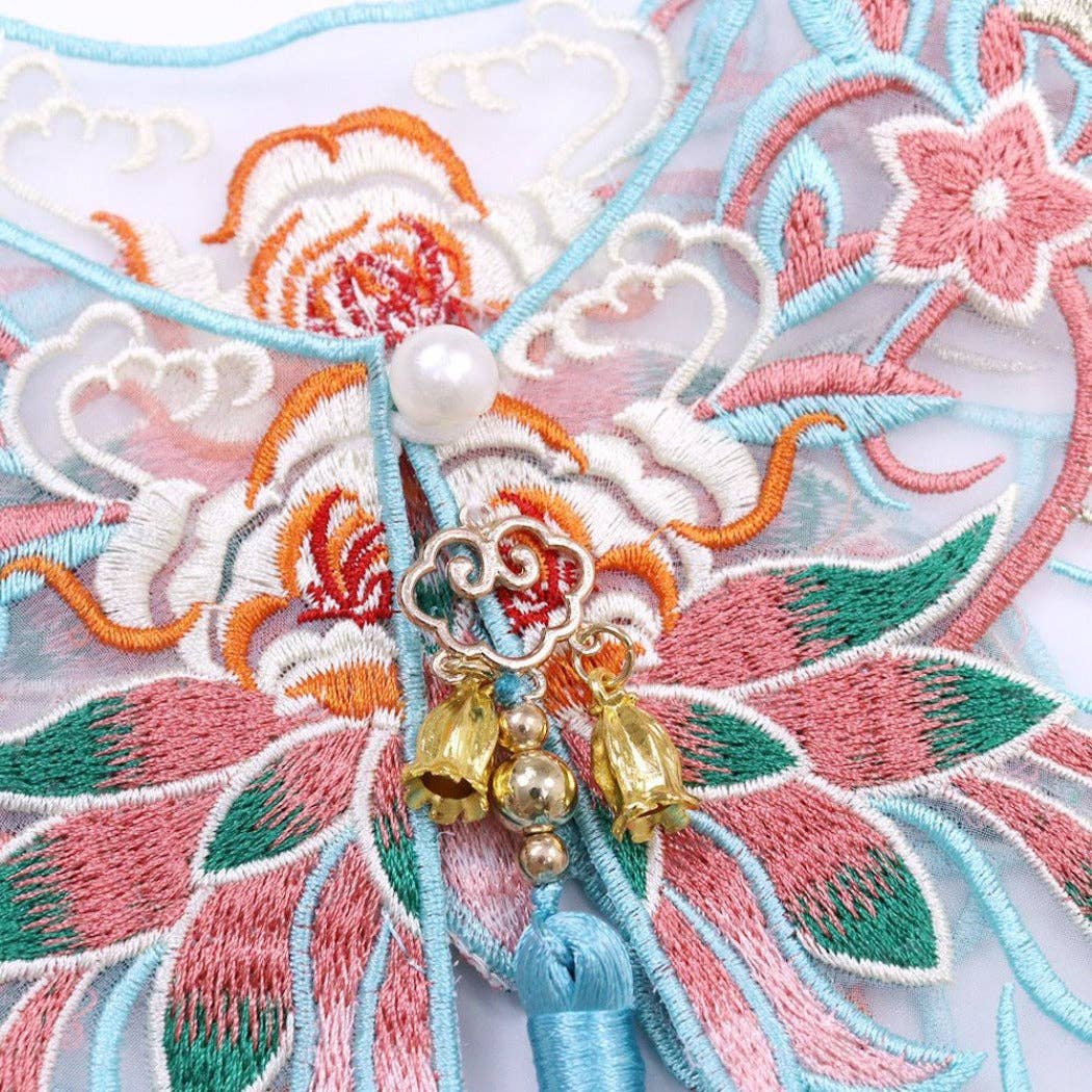 Decorative brooch with floral embroidery and tassels on a textured fabric background