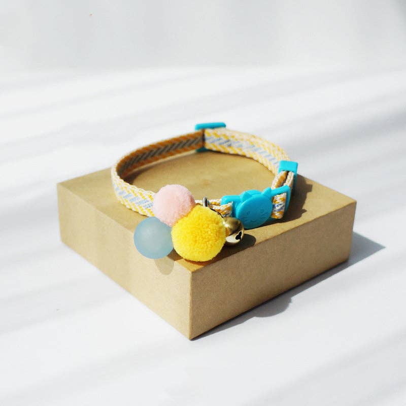 Colorful cat collar with pom-poms on a beige box against a white background